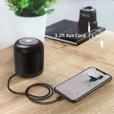 iPhone aux cable connecting an iPhone to a portable speaker via the 3.5mm aux port, demonstrating use on a wooden desk