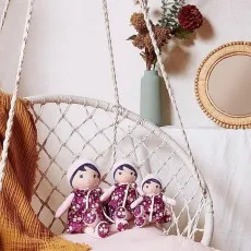 Three purple-dressed Kaloo dolls of varying sizes with floral patterns, sitting together in a white hanging chair