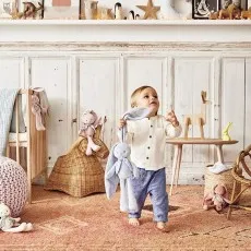 A happy baby holding a blue plush rabbit toy in a nursery.