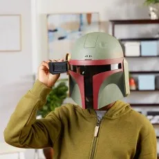 A person wearing a Boba Fett helmet holds the black rangefinder down in front of the visor.