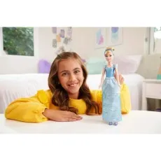 A smiling girl is shown with her hand on a table, next to a Cinderella doll with a blue gown.