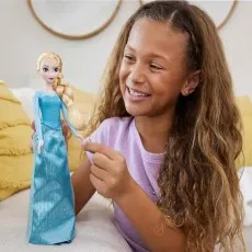 A smiling girl with long, curly hair holds an Elsa doll and gently touches its blonde braid.