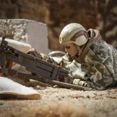 A G.I. Joe Action Soldier figure in a helmet and camouflage poncho, lying down and aiming a machine gun.