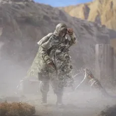 A G.I. Joe Action Soldier figure wearing a camouflage poncho, holding a pistol and looking through dust.