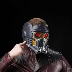 A person wearing a red leather jacket and the Star-Lord helmet points to the side of the mask