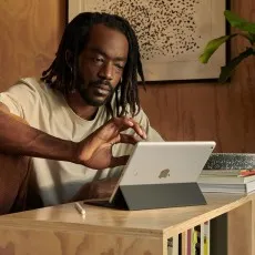 A man sitting at a desk and interacting with an ipad 9th gen 256gb silver that has a keyboard case attached.