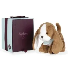 A brown and white plush puppy with floppy ears stands next to a gift box with a burgundy ribbon