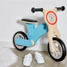 A wooden balance bike with the number 17 on the front stands on a floor with a white rug