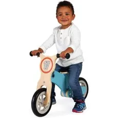 A young child with a big smile rides a wooden Janod balance bike with a light blue frame