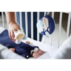 A close-up of a baby sleeping in a crib with a parent's hand holding a soft sheep toy nearby.