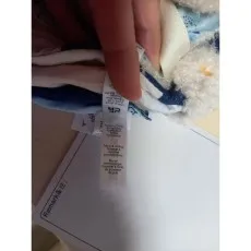 A close-up of a fabric label on a plush toy, detailing that it is made of polyester and recycled fibers.