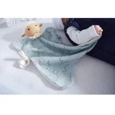 A baby is sleeping in a crib with a light blue security blanket featuring a plush sheep and a pacifier.