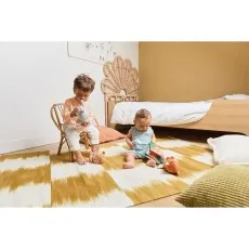 Two young children playing with plush toys on a yellow and white striped rug.