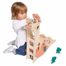 A young child plays with a wooden brontosaurus toy, holding a small dinosaur car at the top of a ramp.