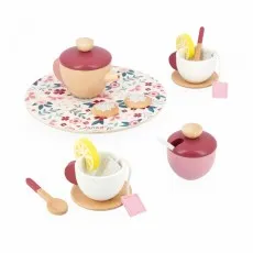 A pink wooden teacup with a tea bag, a spoon, and a lemon slice sits on a round wooden saucer.