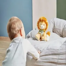 A small child on a wooden floor looks at a plush lion sitting on a striped pillow