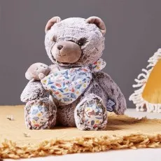 A plush gray teddy bear holding a smaller bear, sitting on a yellow blanket