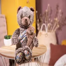 A soft gray bear holding a sleeping brown bear, sitting on a round wooden table