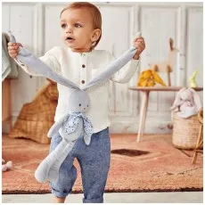 A toddler holds a long-eared plush rabbit by its ears while standing on a rug.