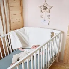 A baby lies in a white crib, with a mobile featuring a teddy bear hanging above them