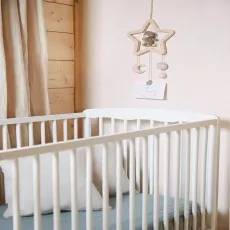 A white baby crib with a wooden mobile featuring a teddy bear hanging above it