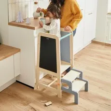 An adult and child use a light wood learning tower to work together at a kitchen counter.