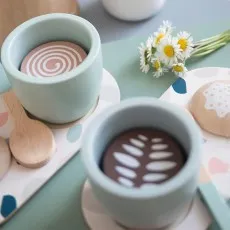 Two wooden toy teacups with spoons and a cookie, arranged for a pretend tea party with daisies.