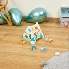 A triangular-shaped wooden toy sorter with animal shapes is on a floor, surrounded by toy animal pieces. Two shiny blue balloons are in the background