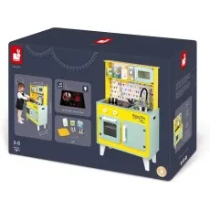 A child plays with a Janod toy kitchen set. The box displays the yellow and mint green wooden kitchen with accessories.