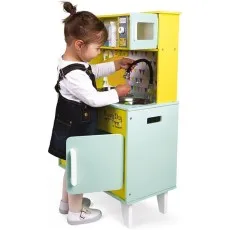 A young child playing with a wooden Janod toy kitchen, holding a pot under the black plastic faucet.