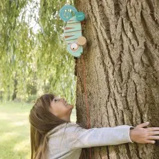 A young girl smiling as she looks up at a wooden chameleon toy on a tree trunk