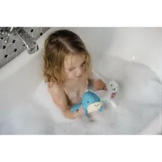 A child in a tub, looking down at a blue whale bath toy she is holding in her hands.