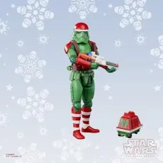 A Star Wars Imperial Stormtrooper action figure in a green and red holiday uniform stands against a snowy background.