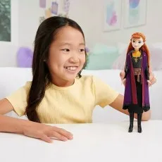 A smiling girl playing with an Anna doll from Disney's Frozen, holding it in her hands.