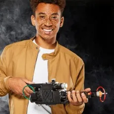 A smiling person with freckles holds a Ghostbusters Proton Pack wand in a smoky room