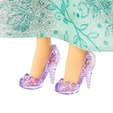 A close-up of a doll's feet wearing transparent purple high-heeled shoes with glitter and seashell details.