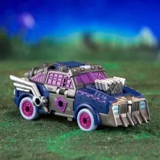 A Transformers Legacy Evolution Axlegrease figure in its vehicle mode, on a background of green grass.