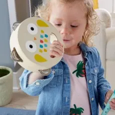 A child shakes a wooden tambourine with an owl's face on it