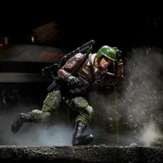 Action figure of a man in combat gear running in a diorama, kicking up dust and debris.