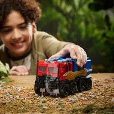 A boy pushing the Optimus Prime figure in its truck mode along a dirt-and-pebble surface