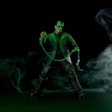 An action figure of Frankenstein's monster in a dynamic pose, holding a chain in a green, smoky room.