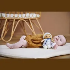 A baby lying on a mat next to a Kaloo soft doll.