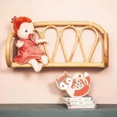 A red-haired doll sitting on a wicker wall shelf, with a small wooden fox toy on books below