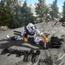 A Storm Shadow figure is doing a split on a rocky surface, with his swords, bow, and other accessories laid out in front of him