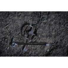 A rusty steel trap with a lever tool and a chain on the ground.