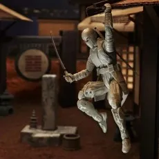 A Storm Shadow action figure in a white ninja outfit, holding a katana and hanging from a rooftop in a diorama setting