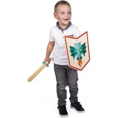 A young boy smiles while holding a wooden toy sword and a shield with a stylized blue dragon