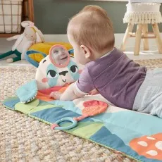 A baby on their stomach during tummy time looking at their reflection in a small mirror attached to a panda pillow