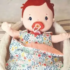 Close-up of a soft cloth doll with red hair and a pacifier, lying in a sherpa-lined floral basket
