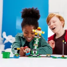 Two kids, a boy and a girl, are excitedly playing with a LEGO Super Mario set on a white table.